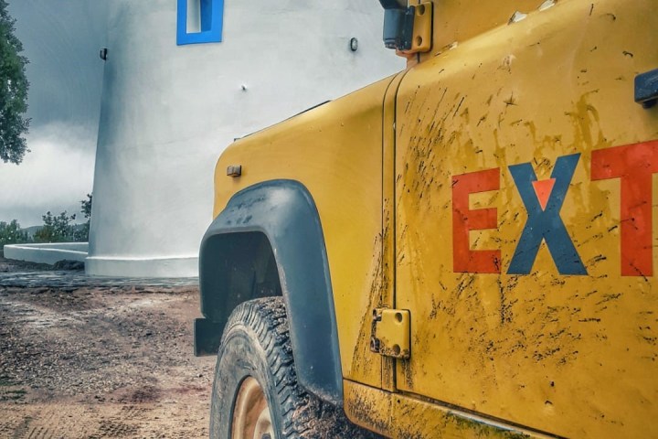 Yellow muddy truck parked near a white cylindrical building with a blue roof.