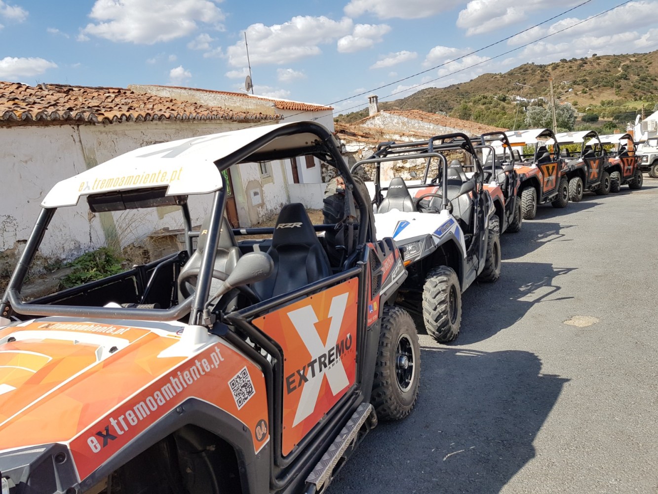 Line of off-road buggies parked on a street under a blue sky with clouds.