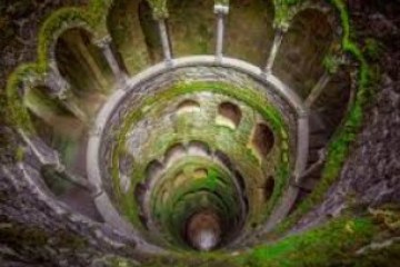 Circular stone structure with arches and moss-covered interior, viewed from above.