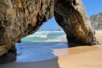 Rock arch framing a sandy beach with waves under a clear blue sky.