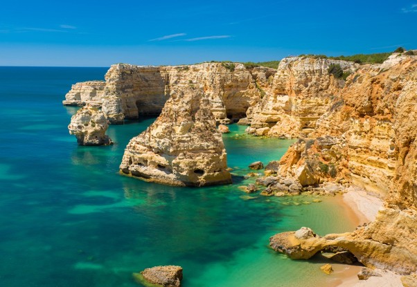 Cliffs with turquoise sea and clear sky, rocky formations and small beach.