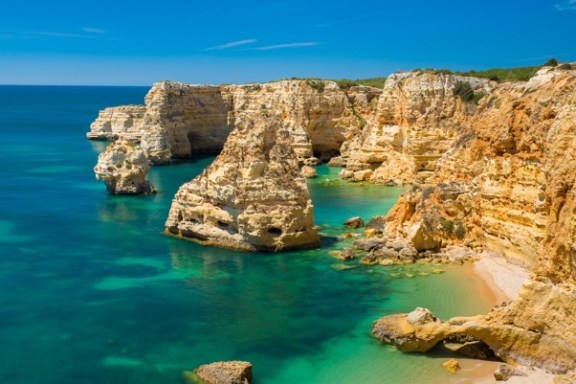 Cliffs with turquoise sea and clear sky, rocky formations and small beach.