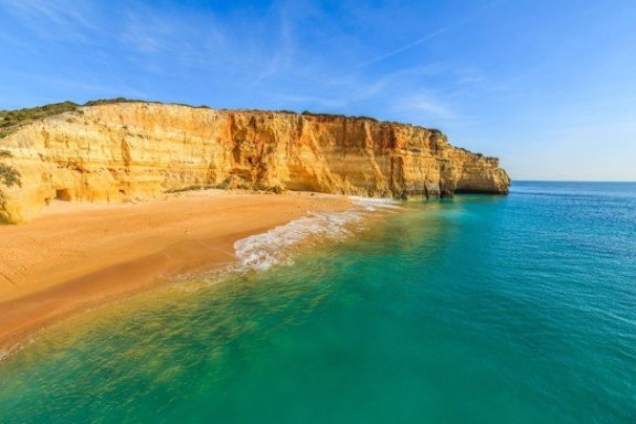 Cliffside beach with turquoise water, sandy shore, and clear blue sky.