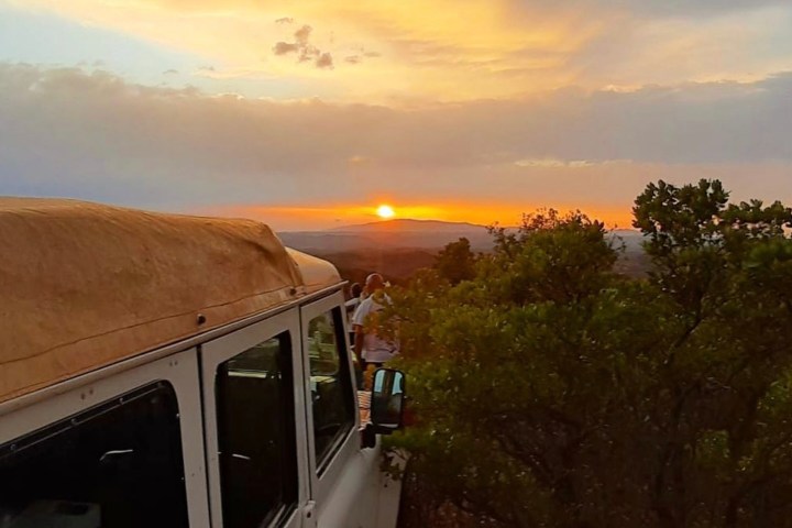 White SUV with rooftop tent near bushes at sunrise with cloudy sky.