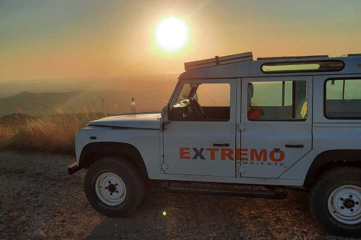 White off-road vehicle on a hilltop at sunset with a clear sky.