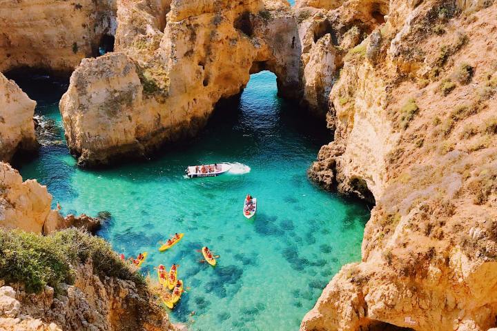 Turquoise water surrounded by rocky cliffs with boats and kayaks in a coastal cove.