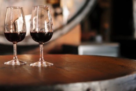 Two wine glasses with red wine on a wooden table in a dimly lit setting.