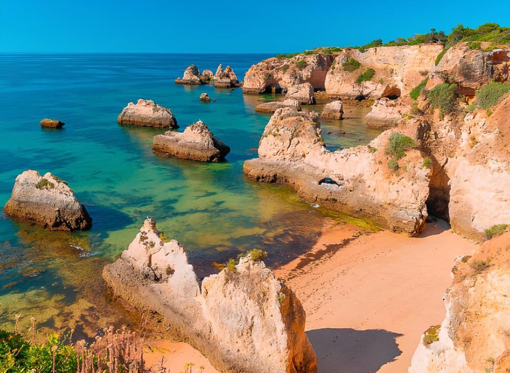 Scenic beach with rock formations, clear blue water, and sandy shore under a bright blue sky.