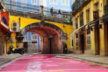 Colorful alley with pink pavement, yellow buildings, and archway featuring a parked motorcycle.