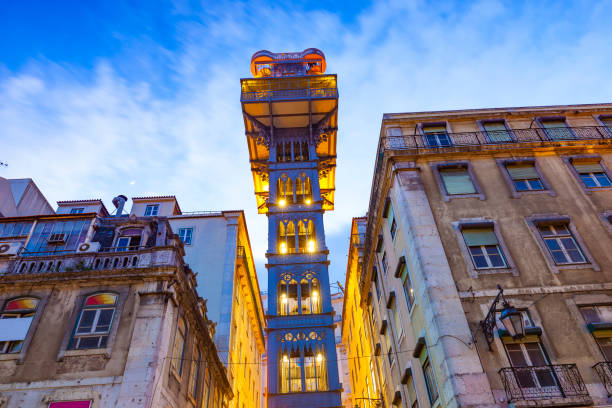 Illuminated metal elevator tower between old buildings at dusk.