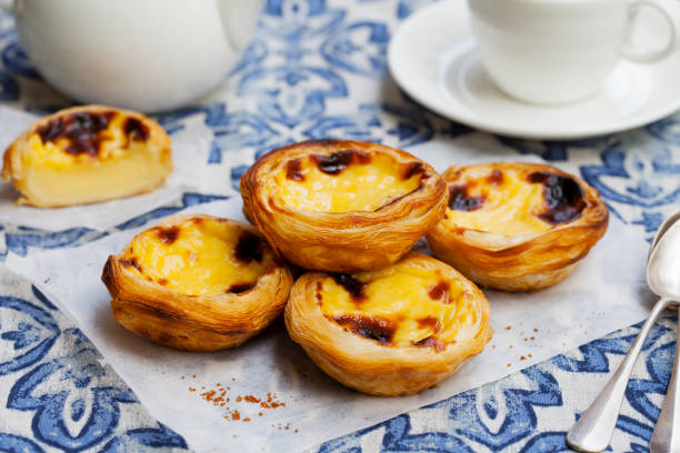 Four custard tarts on a blue patterned cloth with a teapot and cup in the background.