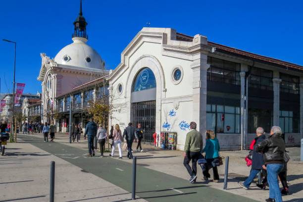 People walking by a historic market building with a dome on a clear day.
