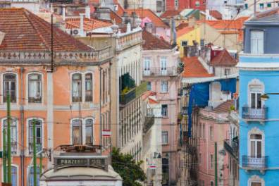 Yellow tram on cobblestone street with colorful buildings and cloudy sky in the background.