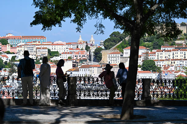 Silhouetted people under trees overlooking colorful hillside cityscape.