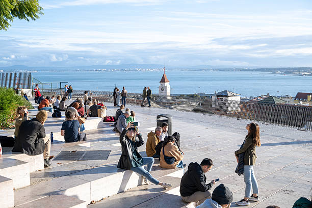 People relaxing on a terrace with ocean view and cityscape in the background under a blue sky.