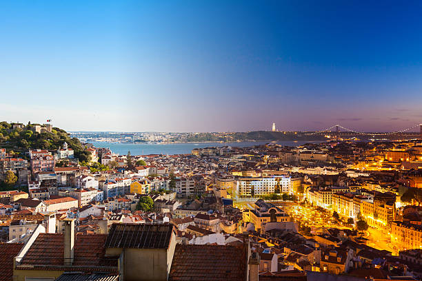 Lisbon cityscape at twilight with illuminated streets and a view of the river and bridge.
