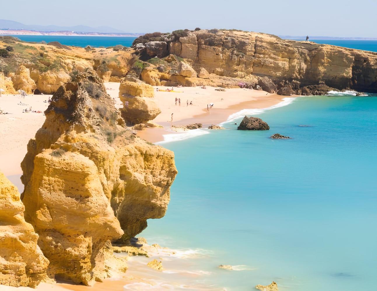 Scenic beach with rocky cliffs, turquoise water, and sunbathers.